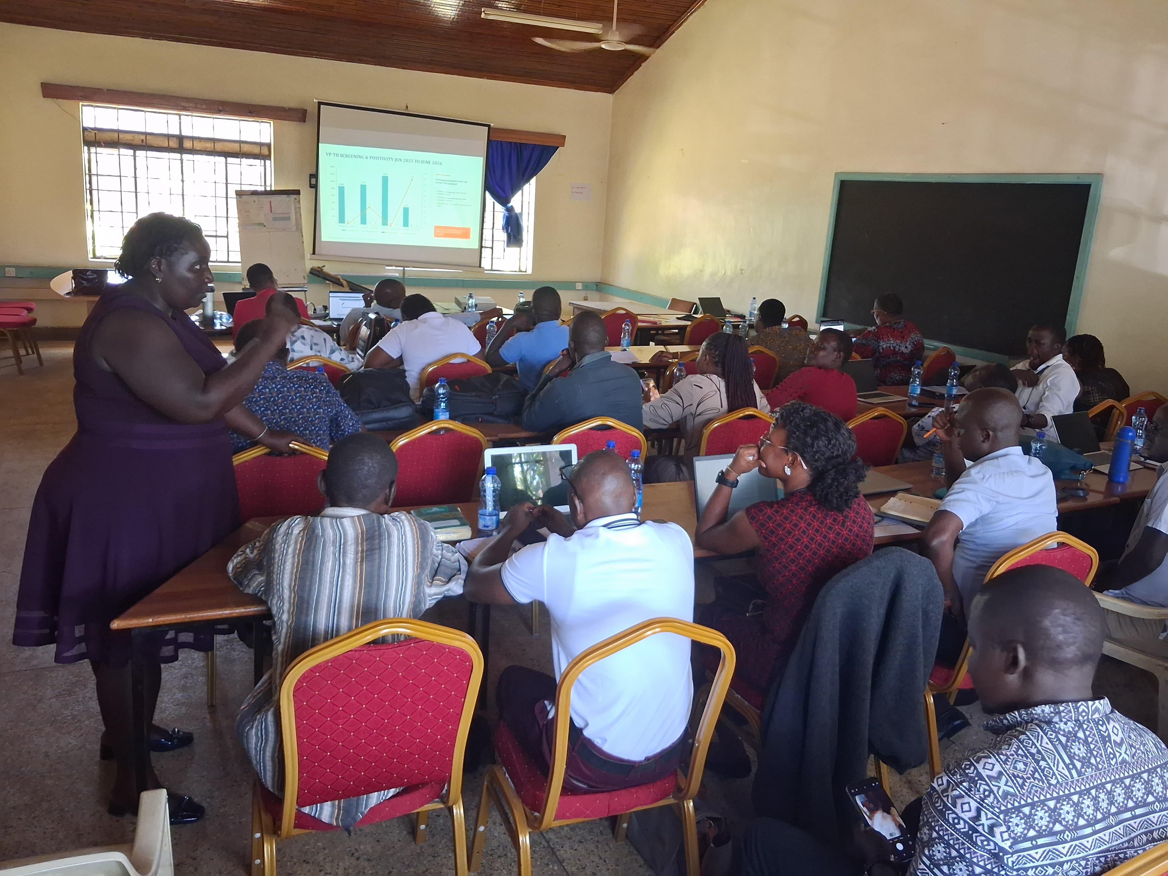 Participants with laptops and notebooks seated at tables listening during the County Key and Vulnerable Populations Technical Working Group meeting at KCRH Hall